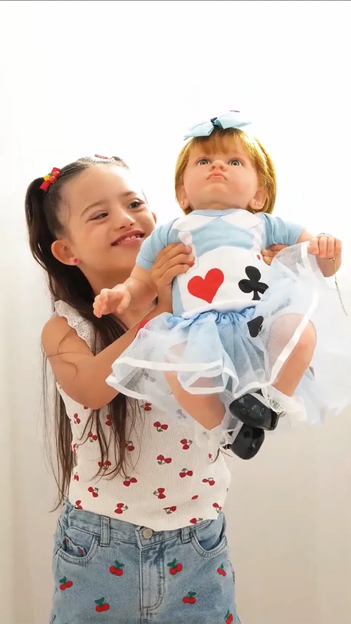 Menina sorrindo enquanto segura uma bebê reborn inspirada em Alice