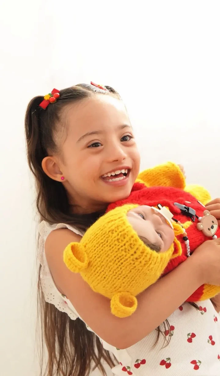 Menina abraçando um bebê reborn com fantasia inspirada no Ursinho Pooh
