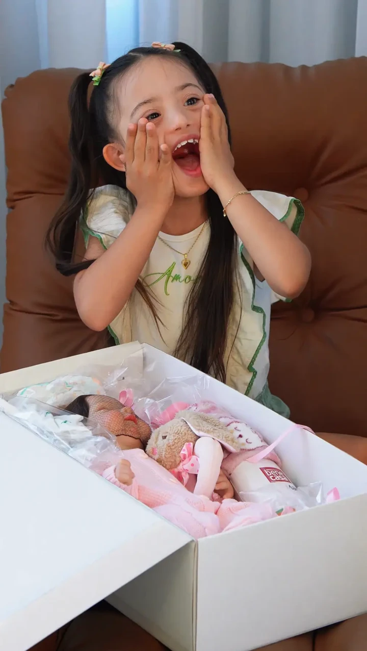 Menina emocionada ao abrir uma caixa com um bebê reborn e seu enxoval